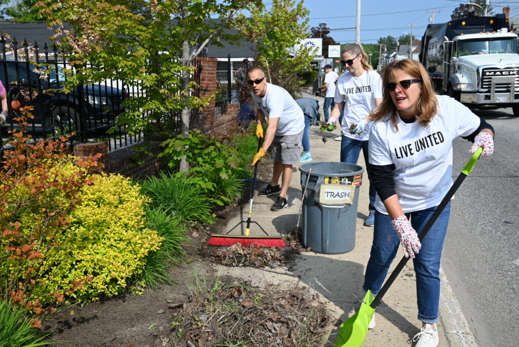 Volunteers clean planting beds along the sidewalk and fence at Sweetser's Sanford office.