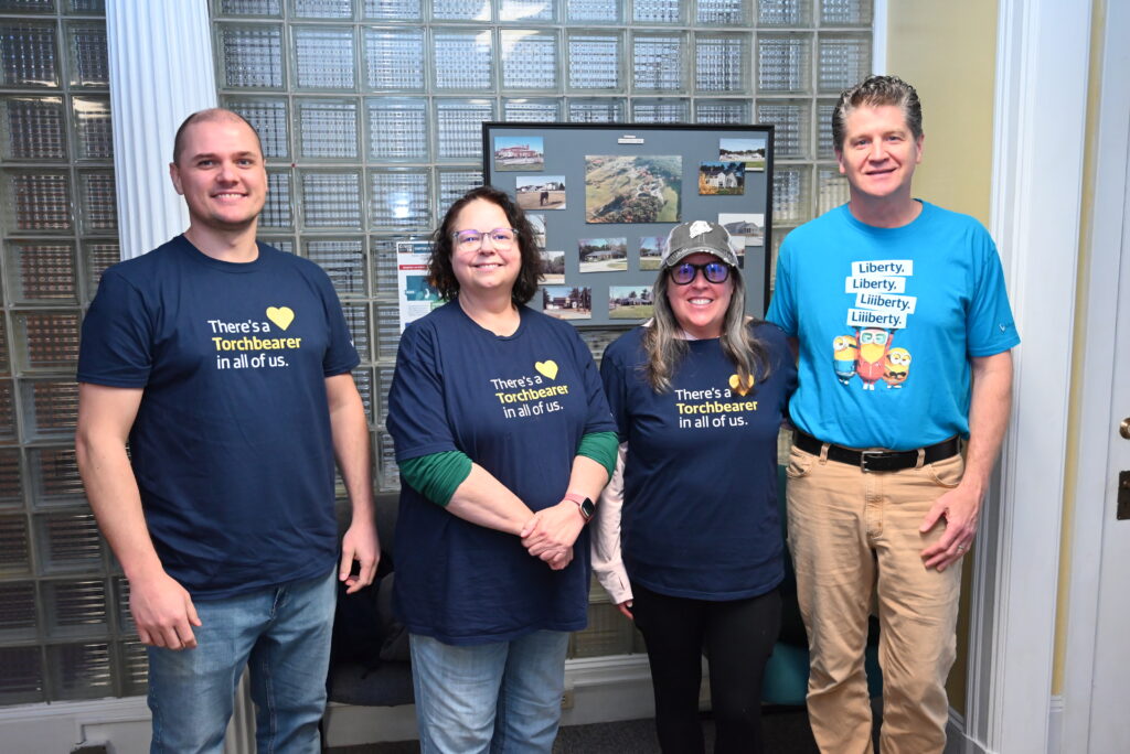 Four volunteers pose together in a building on the Saco Campus.